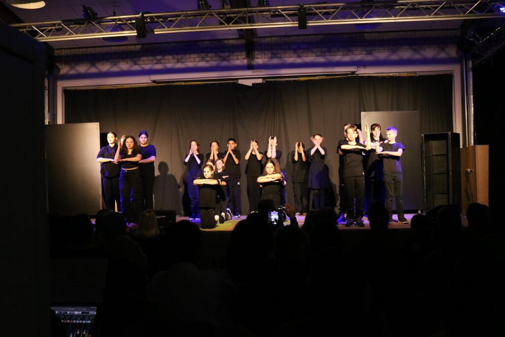 Schüler führen auf einer Bühne eine Theateraufführung auf.