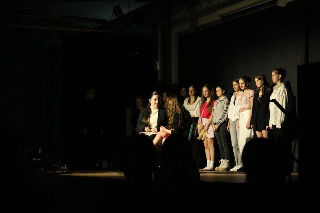Gruppe von Schülern auf einer Bühne während einer Aufführung in gedämpftem Licht.