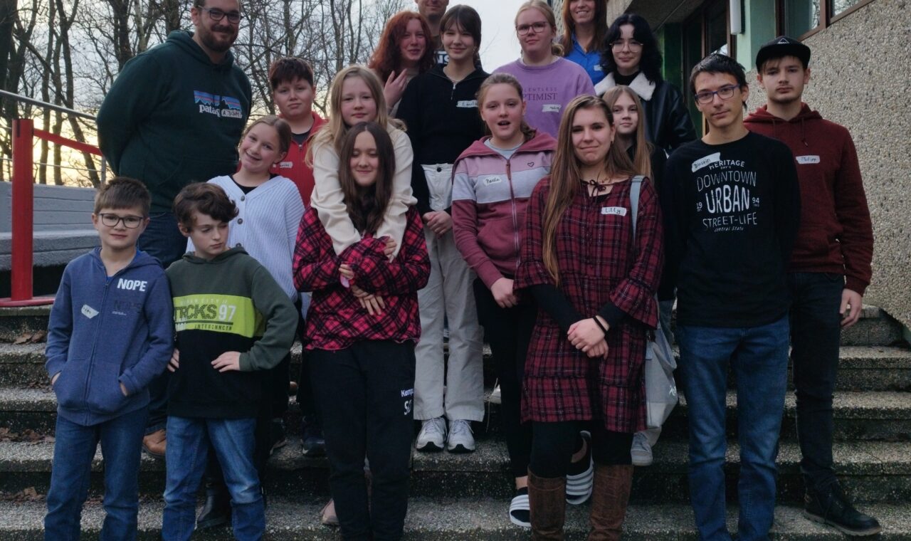 Gruppe von Schülern und Lehrern vor einem Schulgebäude auf Treppenstufen.