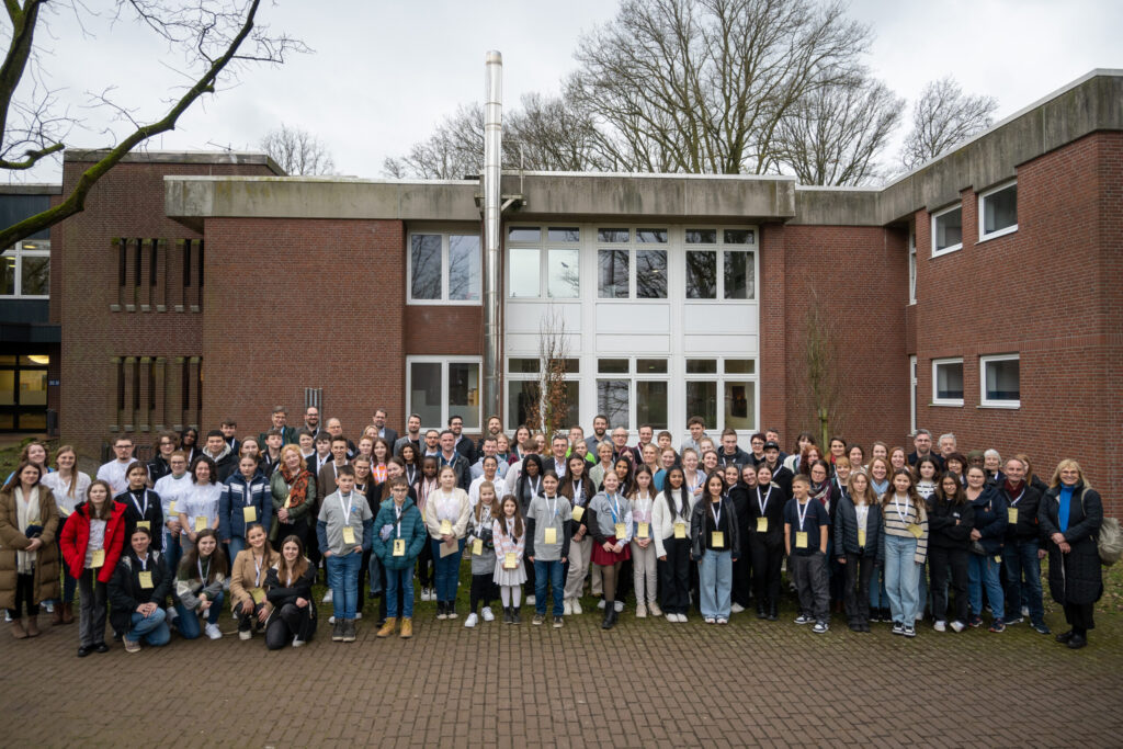 Gruppenfoto vor einem Gebäude mit vielen Menschen in unterschiedlichen Kleidung.