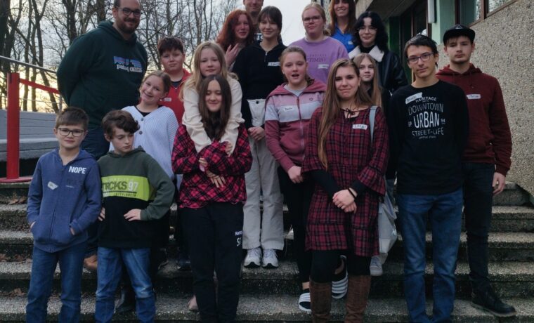 Gruppe von Schülern und Lehrern vor einem Schulgebäude auf Treppenstufen.