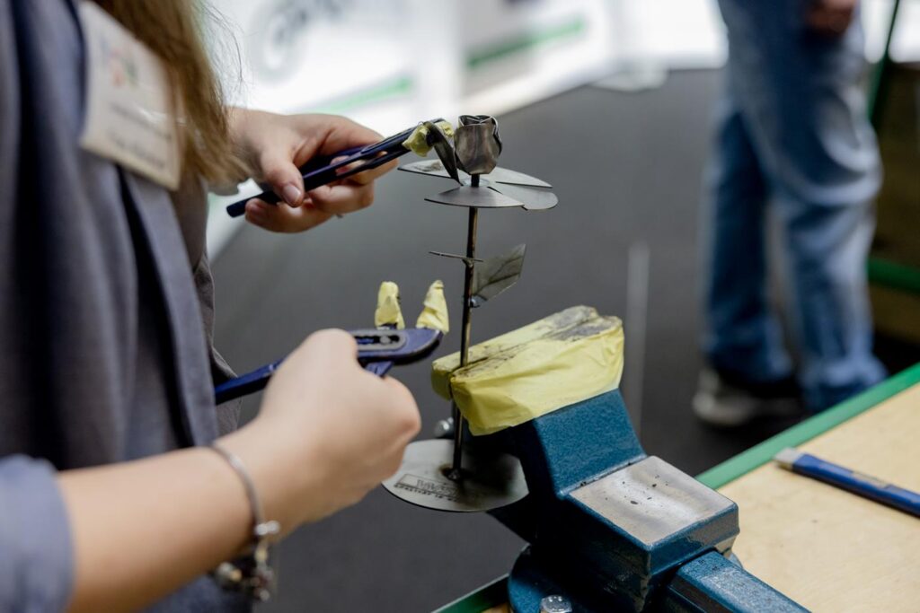 Eine Person arbeitet an einem Metallobjekt, das im Schraubstock fixiert ist.