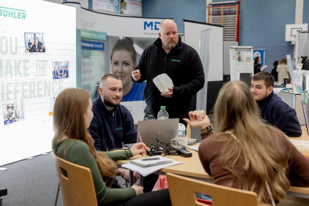 Berater spricht mit mehreren Personen an einem Messestand.