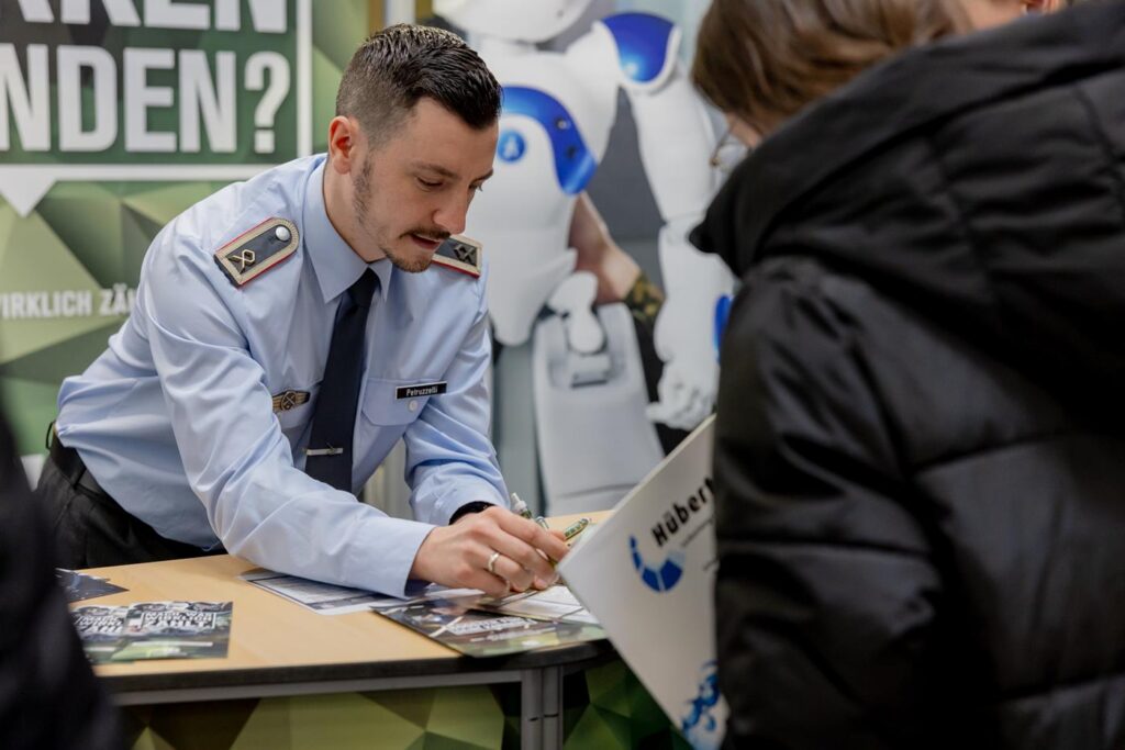 Ein Polizist erklärt Informationen an einem Stand, im Hintergrund ein Roboter.