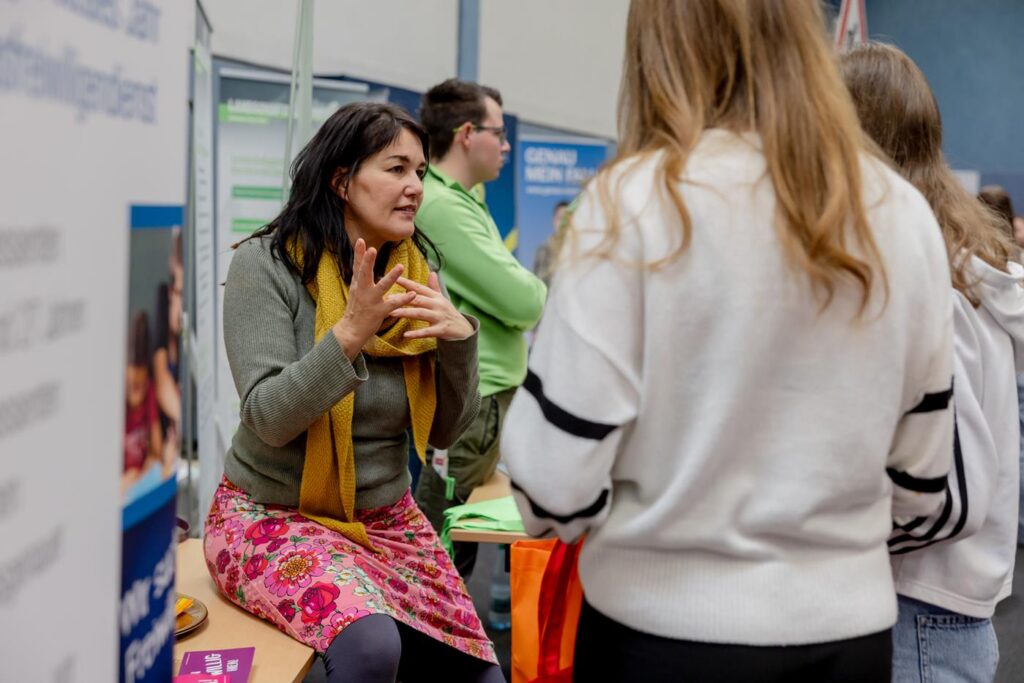 Frau spricht mit Besuchern an einem Informationsstand.