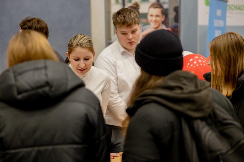 Schülerinnen und Schüler stehen an einem Tisch und sprechen mit Besuchern.