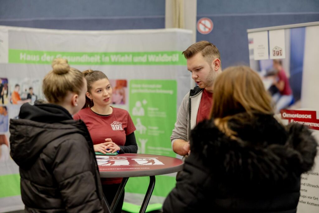 Messestand mit zwei Personen, die Informationen an Besucher überreichen.