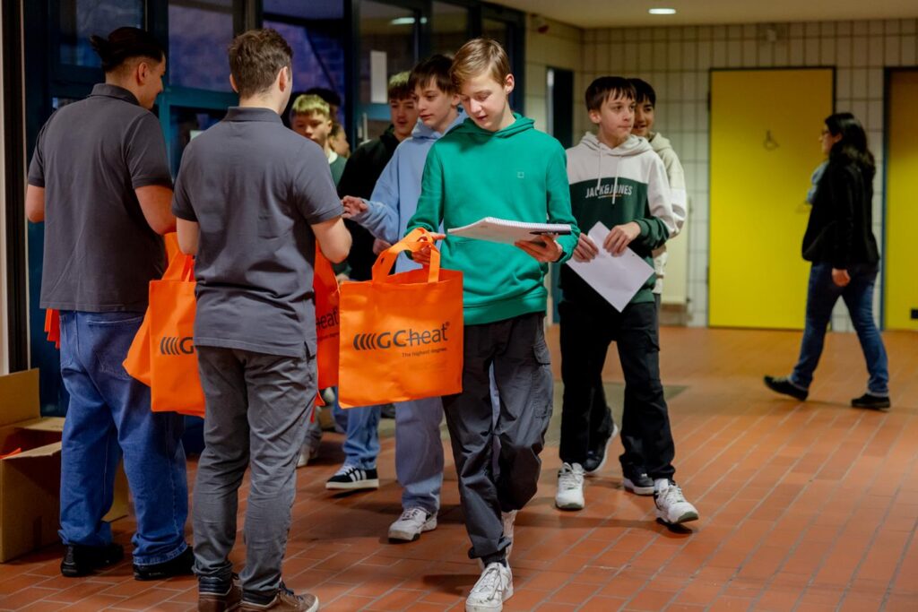 Schüler erhalten orangefarbene Taschen und Broschüren im Eingangsbereich der Schule.