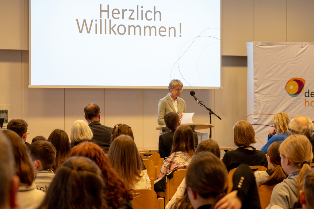 Frau spricht zu einem Publikum bei einer Begrüßungsveranstaltung.