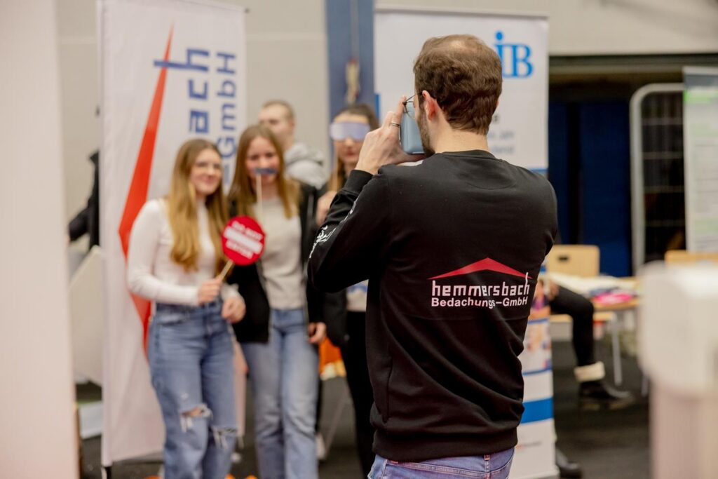 Junge Leute posieren für ein Foto an einem Stand auf einer Veranstaltung.
