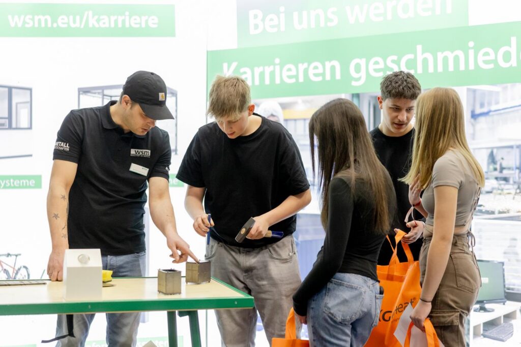 Mitarbeiter erklärt während einer Messe verschiedene Materialien einer Gruppe von Interessierten.