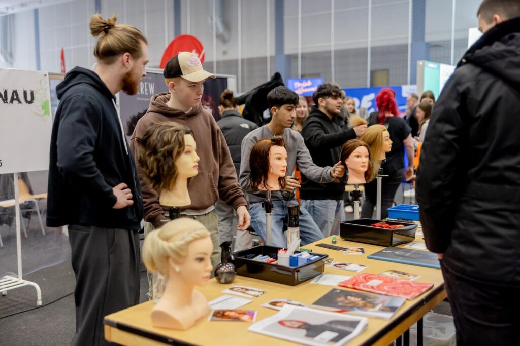 Teilnehmer betrachten Frisuren an Schaufensterpuppen auf einem Messe-Stand.