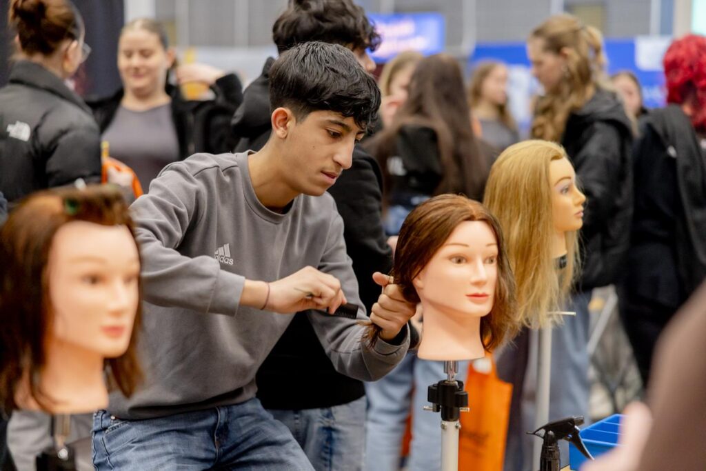 Schüler frisiert eine Übungspuppe an einem Frisiersalon-Stand.