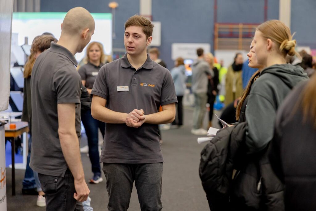 Zwei junge Männer in T-Shirts sprechen mit einer Frau auf einer Messe.