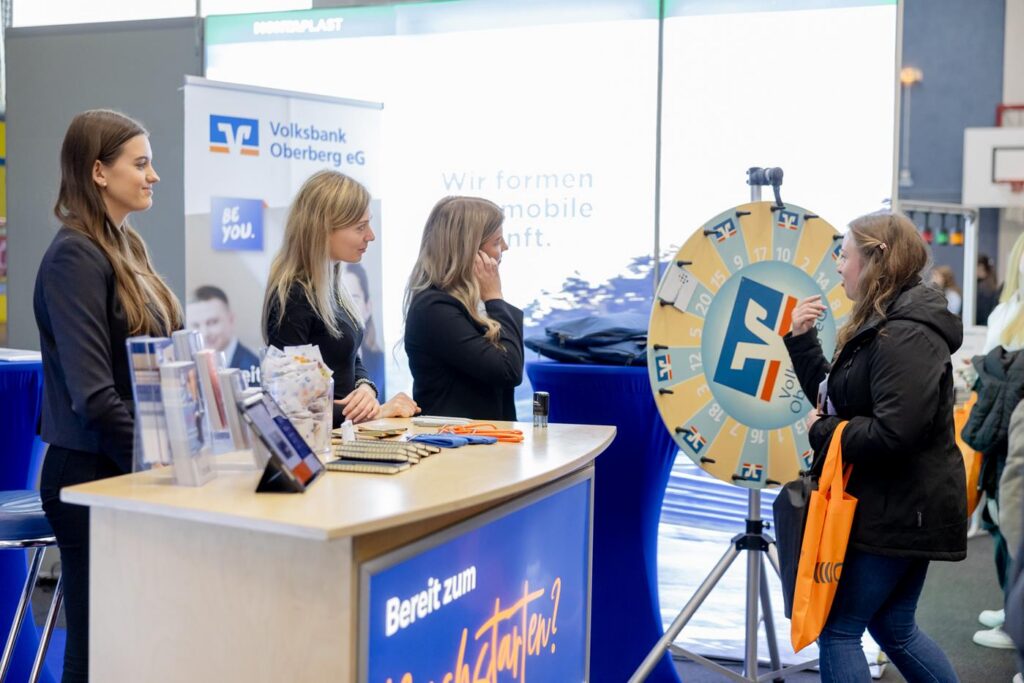 Messe-Stand mit drei Frauen und einem Glücksrad. Besucherinteraktion.
