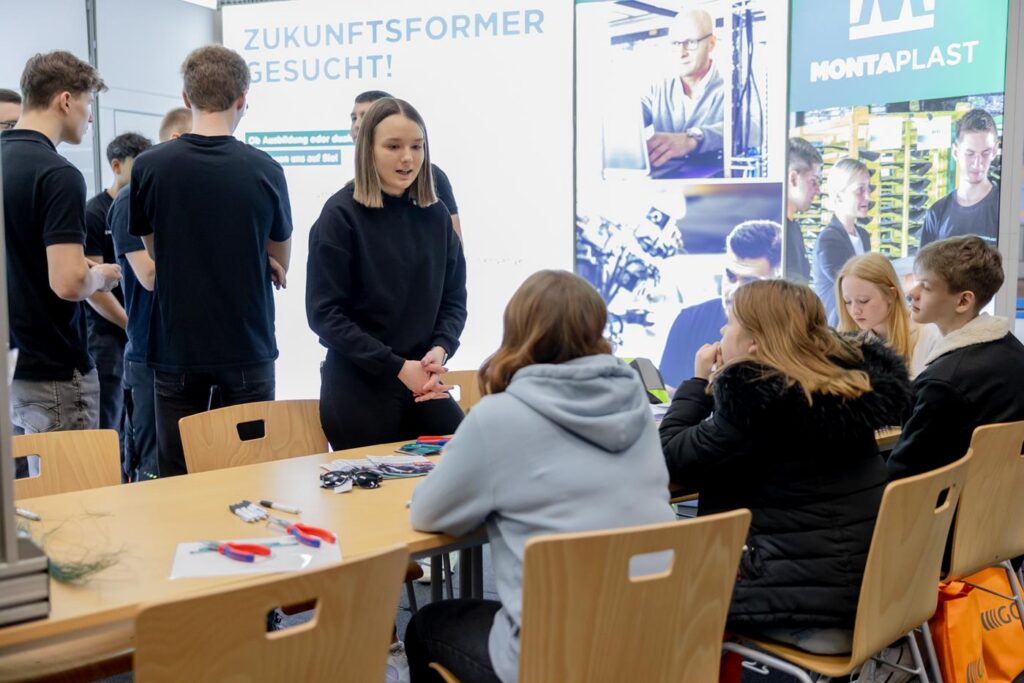 Berufsmesse mit Schülerinnen und Schülern, die Informationen von einer Mitarbeiterin erhalten.