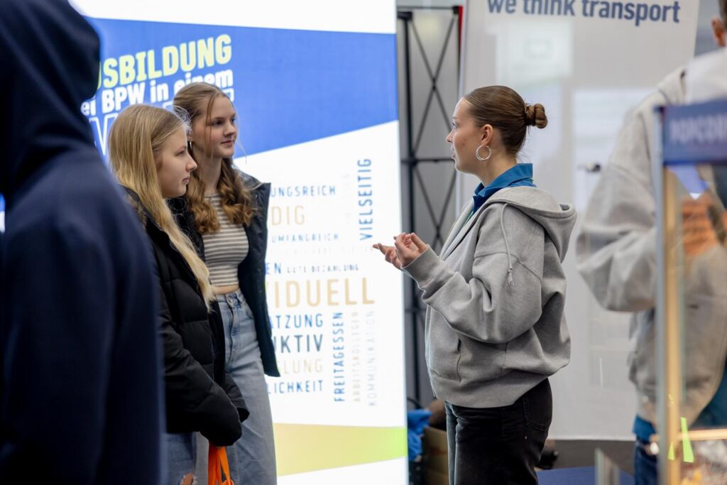 Mädchen stehen an einem Stand und sprechen mit einer Beraterin.