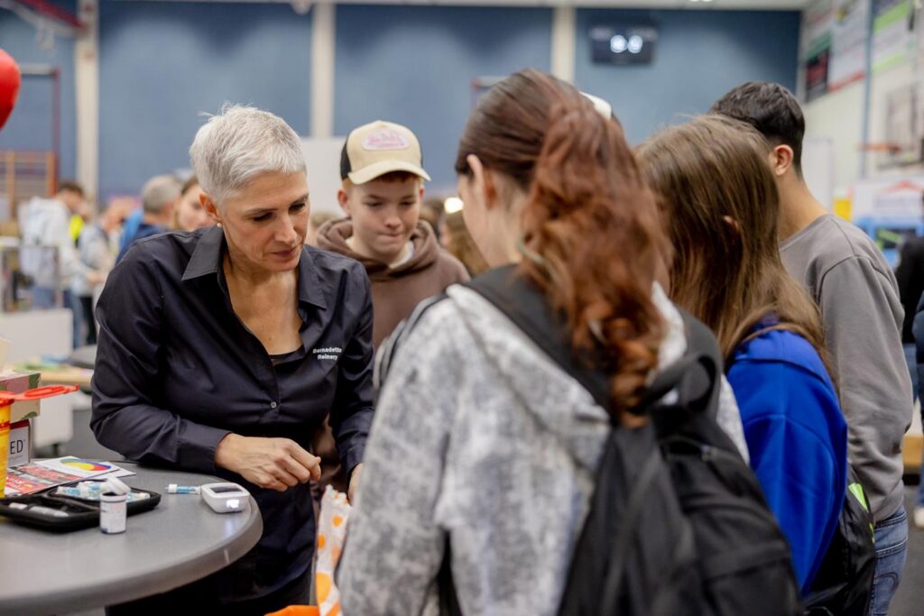 Eine Frau spricht mit mehreren Jugendlichen an einem Stand.