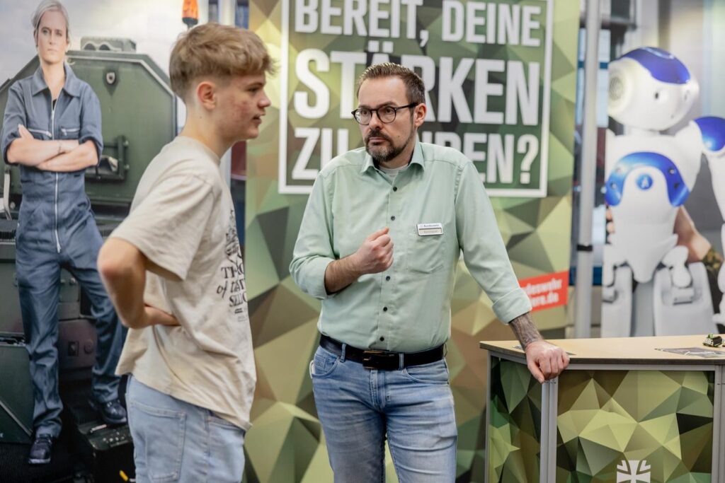 Zwei Personen im Gespräch vor einem Informationsstand mit diversen Plakaten.