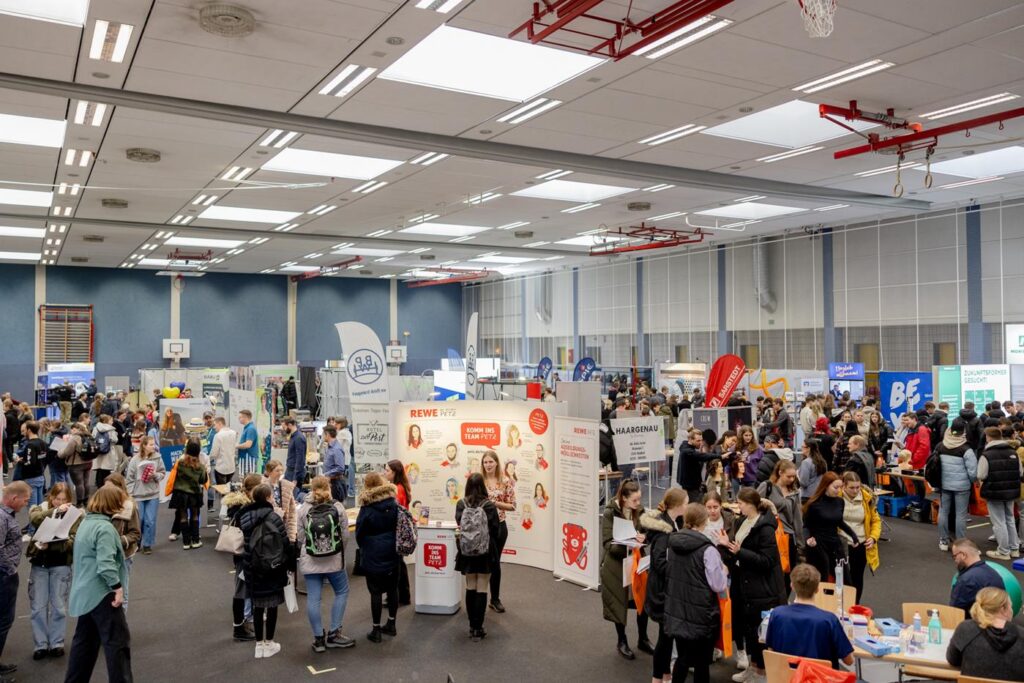 Menschenmenge auf einer Messe mit verschiedenen Ständen und Informationsangeboten.