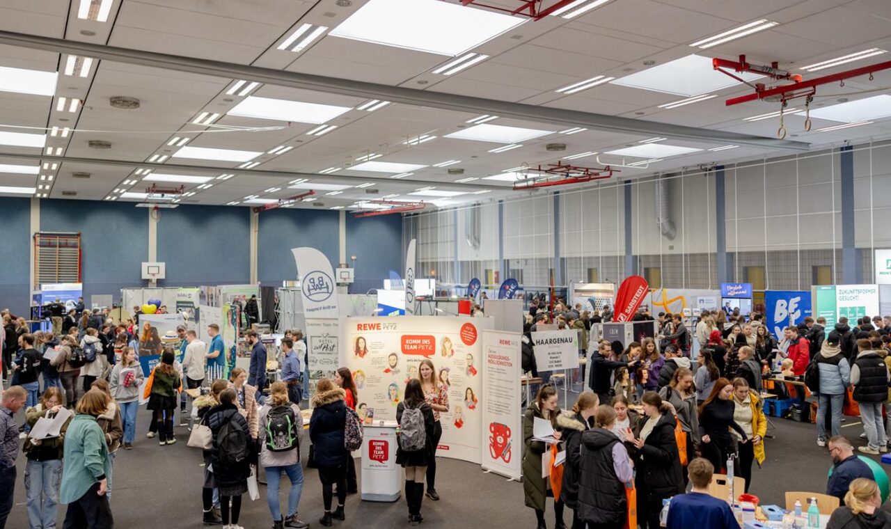 Menschenmenge auf einer Messe mit verschiedenen Ständen und Informationsangeboten.