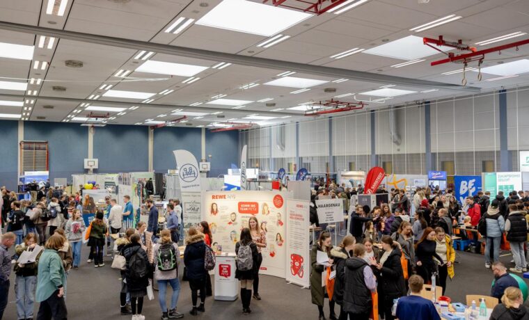 Menschenmenge auf einer Messe mit verschiedenen Ständen und Informationsangeboten.
