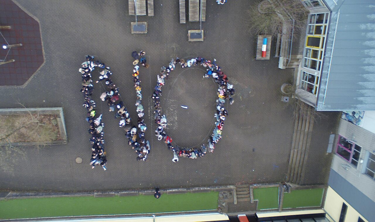 Schüler stehen im Freien und bilden das Wort "NO".