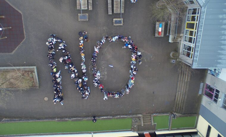 Schüler stehen im Freien und bilden das Wort "NO".
