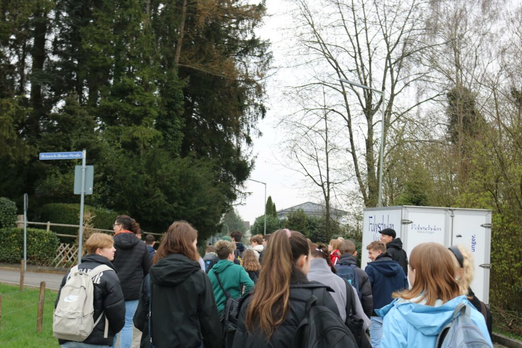 Schüler gehen gemeinsam einen Weg entlang, Bäume und ein Wohngebiet im Hintergrund.