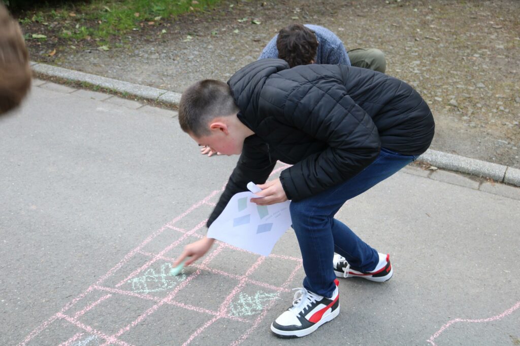 Schüler zeichnen mit Kreide auf dem Boden und arbeiten an einer Aufgabe.