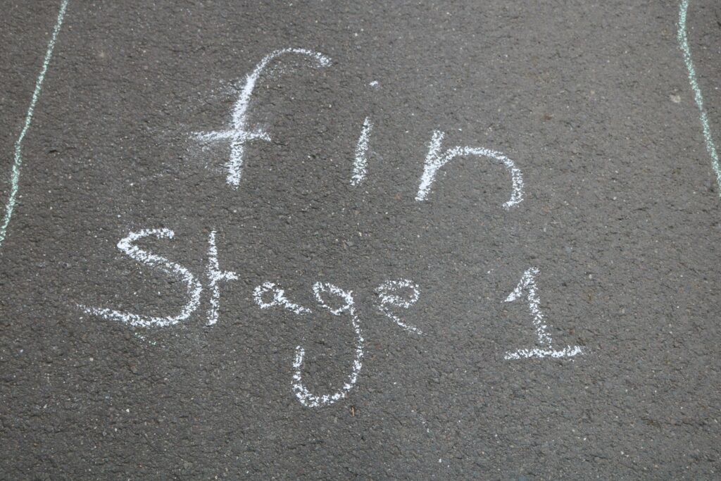 Schwarzer Asphalt mit Kreideinschrift "fin Stage 1".