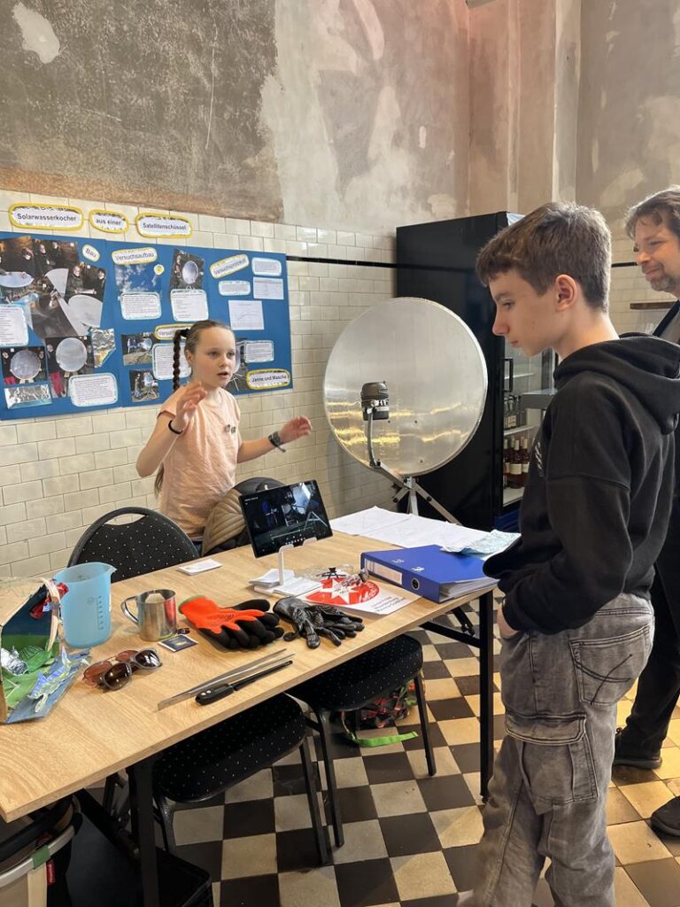 Schüler präsentiert Experimente an einem Tisch mit verschiedenen Materialien.