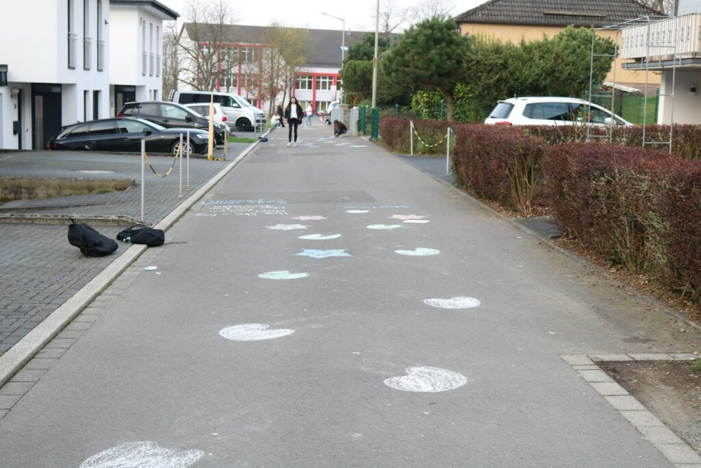 Schulweg mit bunten Kreisen auf dem Asphalt und Personen im Hintergrund.