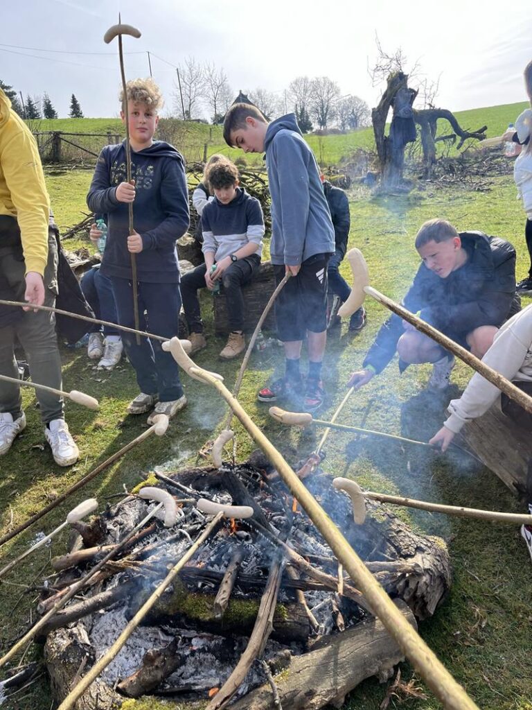 Gruppe von Jugendlichen, die um ein Lagerfeuer sitzt und Stockbrot zubereitet.