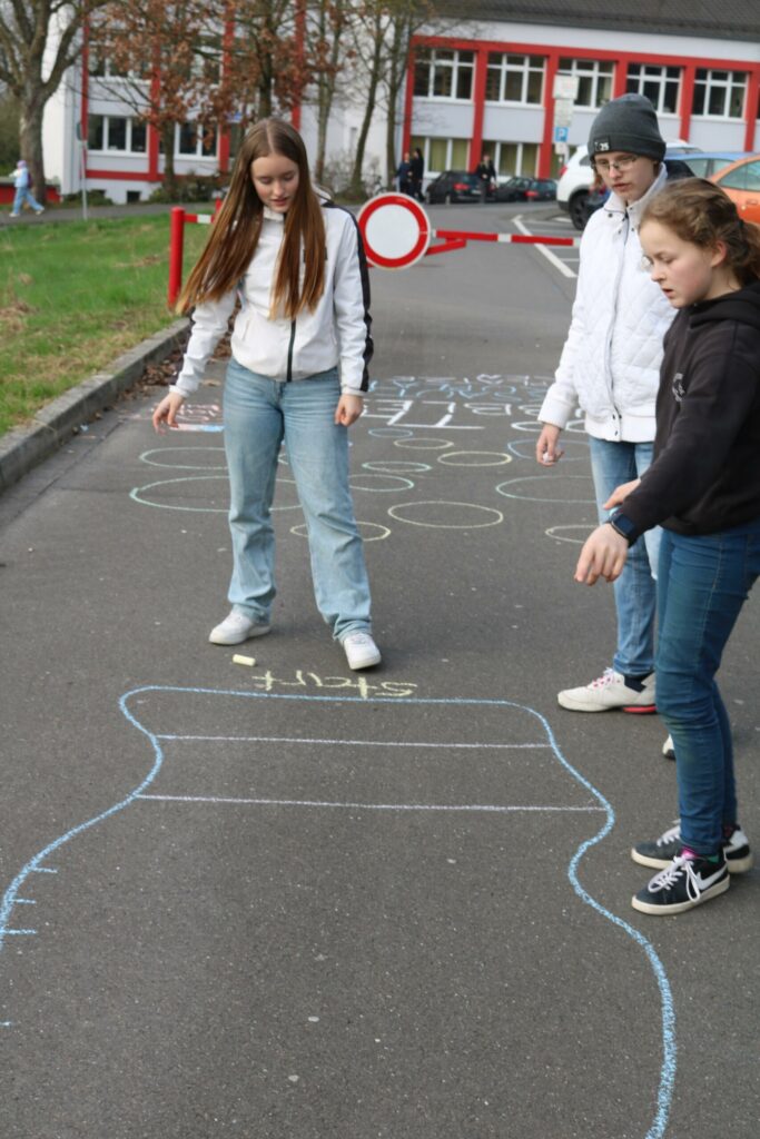 Schüler spielen im Freien auf einer mit Kreide gezeichneten Spielfläche.