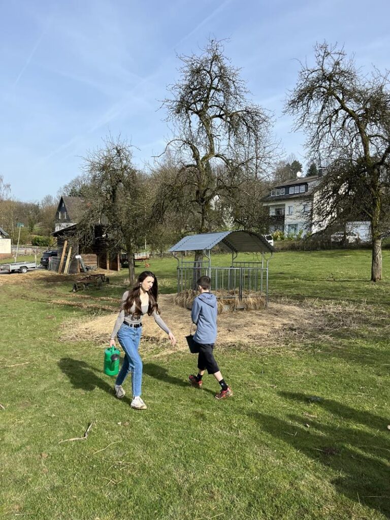 Kinder laufen auf einem Wiesenstück in Richtung eines Gartenhauses.