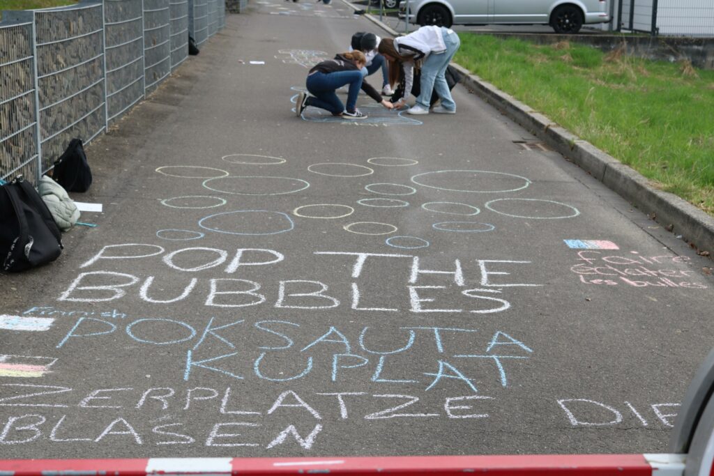 Kinder zeichnen mit Kreide auf einem Gehweg, umgeben von Fahrzeugen.