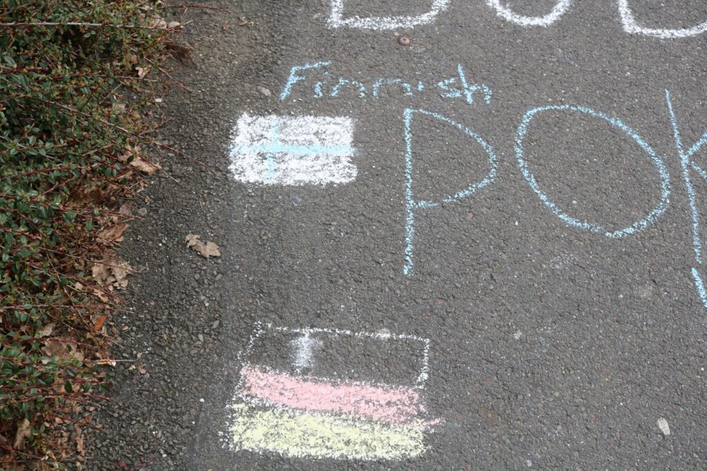 Bunte Kreidezeichnungen auf Asphalt, darunter Fahnen und Schriftzüge.
