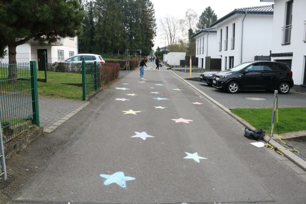 Bunte Sterne auf einer Straße, Spaziergänger und Autos im Hintergrund.