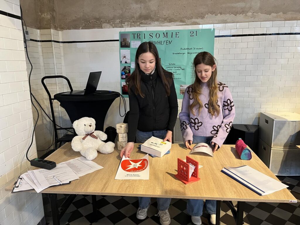 Zwei Schülerinnen stehen an einem Tisch mit Büchern und Materialien.