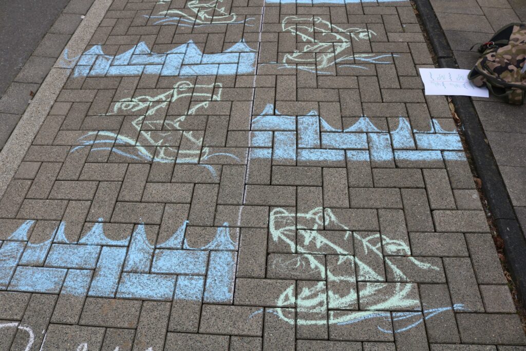 Bunter Strich auf dem Gehweg zeigt Froschfiguren und Wellen.