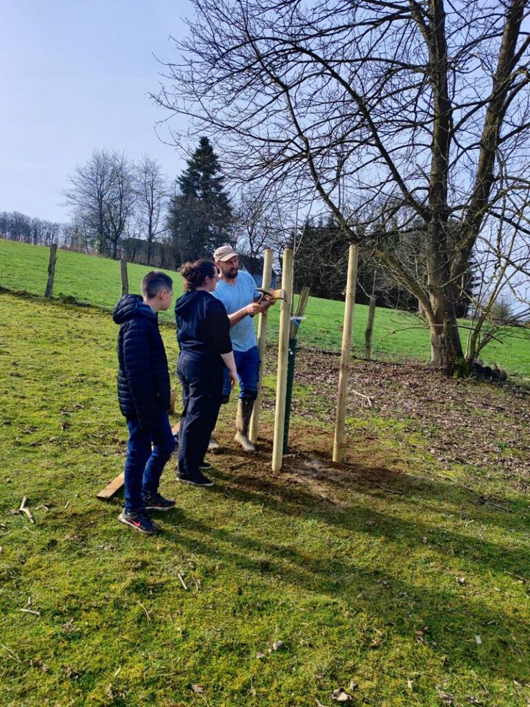 Drei Personen stehen im Freien und arbeiten an einem Holzgestell.