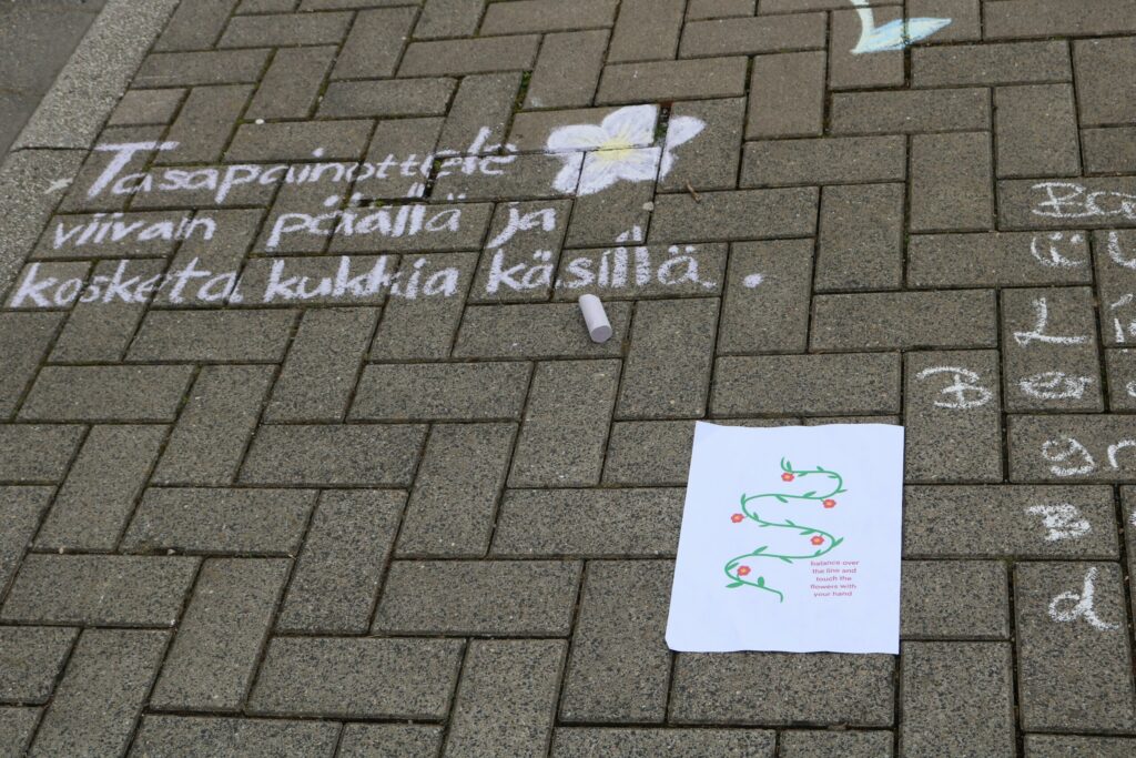 Graue Pflastersteine mit bunten Kreidezeichnungen und einem handgeschriebenen Text.
