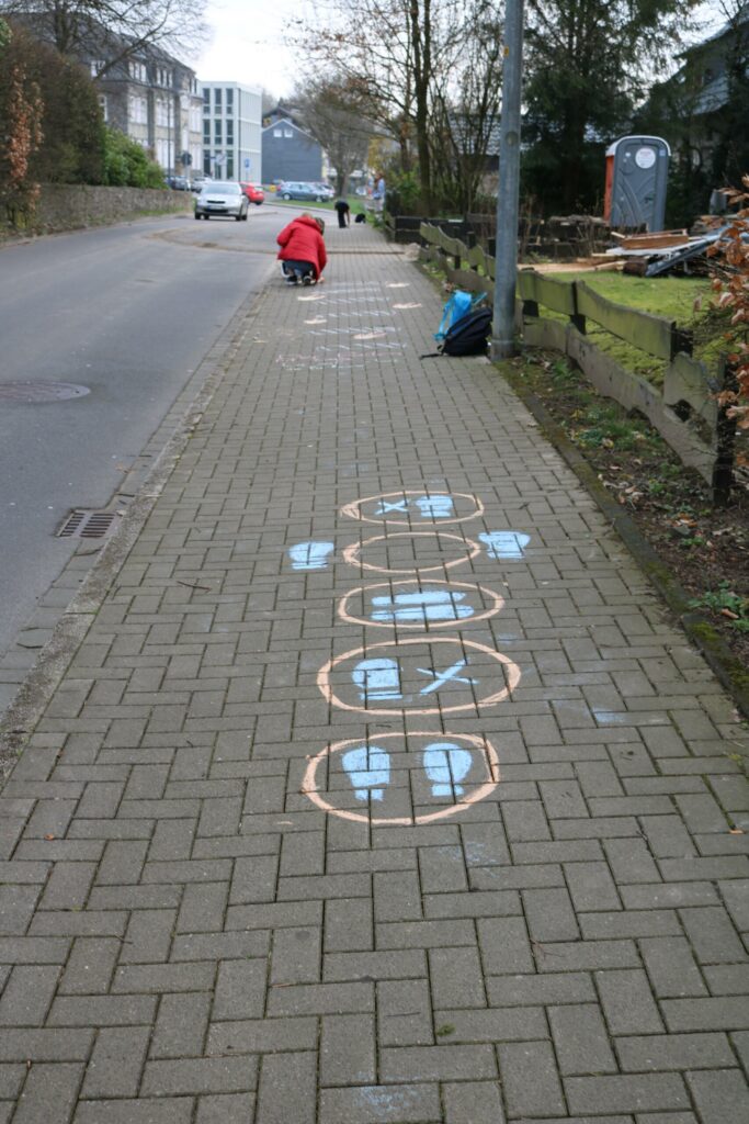 Blick auf einen Gehweg mit aufgemalten Zahlen und Formen für ein Spiel.