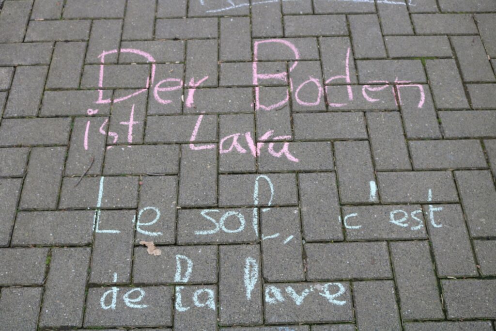 Boden mit bunten Kreidebeschriftungen in deutscher und französischer Sprache.