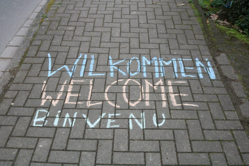 Bunte Willkommensschriftzüge auf einem Kopfsteinpflasterweg.