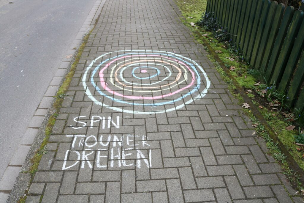 Bunte Kreise aus Kreide auf einem Gehweg mit dem Text „Spin Trouner drehen“.