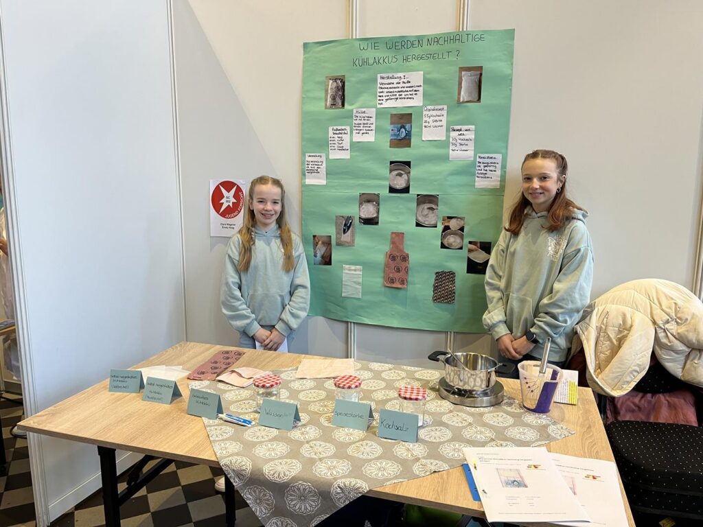 Zwei Mädchen stehen an einem Tisch mit einem Plakat und Materialien für ein Projekt.
