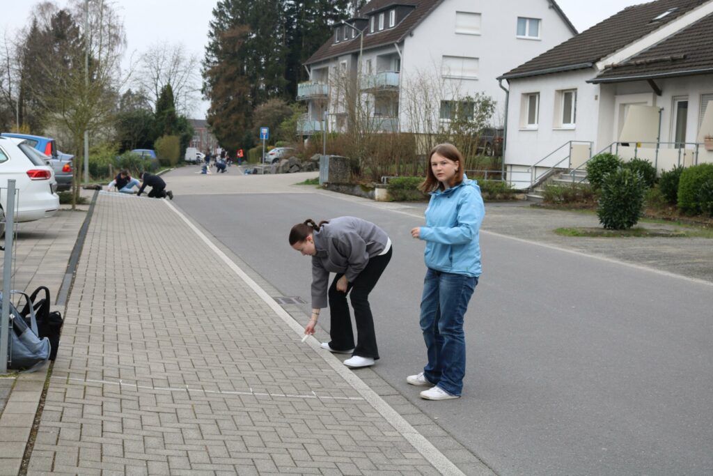 Zwei Personen reinigen den Gehweg auf einer ruhigen Straße.