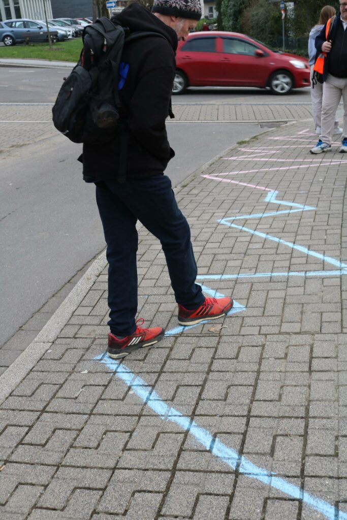 Schüler steht auf einem mit Kreide gezeichneten Weg auf dem Gehweg.
